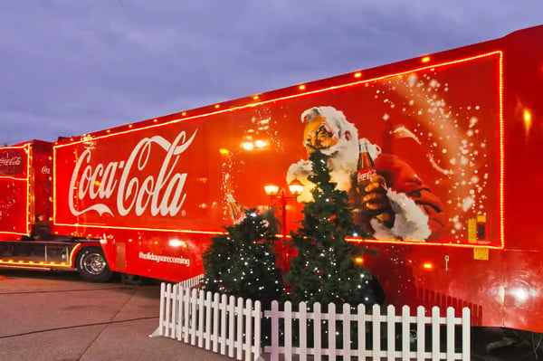 Sur cette photo, un camion coca cola avec un décor de noël et le père noël qui tient une bouteille de coca 