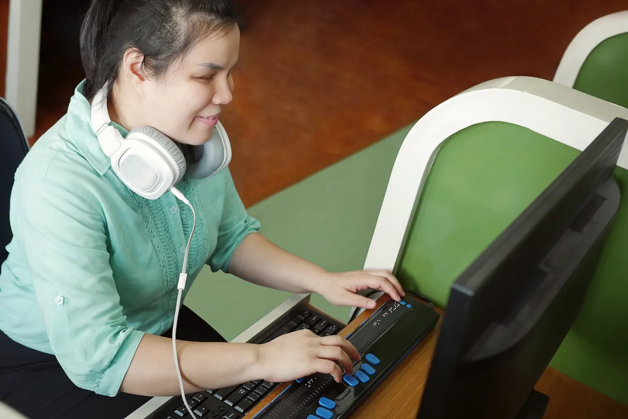 Sur la photo, une jeune fille malvoyante saisit un texte sur ordinateur à l'aide d'un clavier adapté
