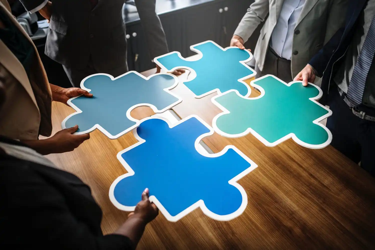 Quatre personnes tiennent des pièces de puzzle colorées qui s'emboîtent pour former un ensemble cohérent. Cette image symbolise la collaboration et l'intégration des différentes parties du marketing automation pour créer une stratégie efficace.